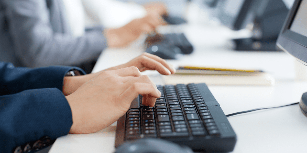 Business professionals practicing touch typing techniques at keyboards in a Canadian office, demonstrating proper hand placement for WPM typing certification preparation.